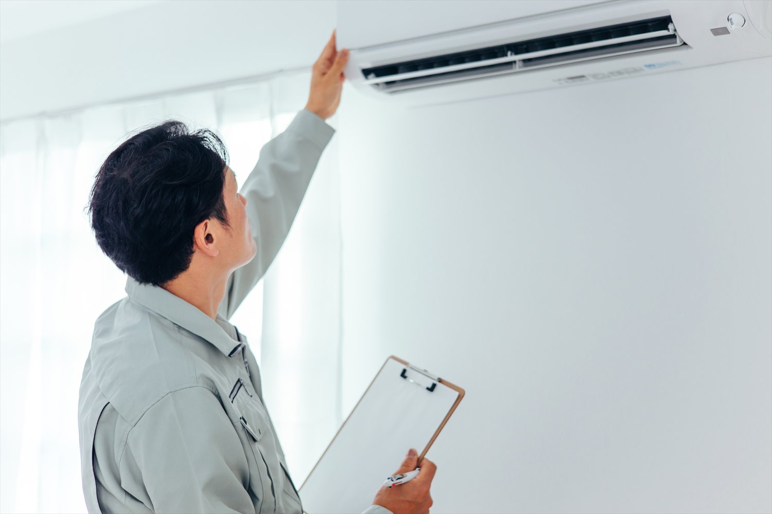 エアコン・空調設備のチェックをする作業着の男性